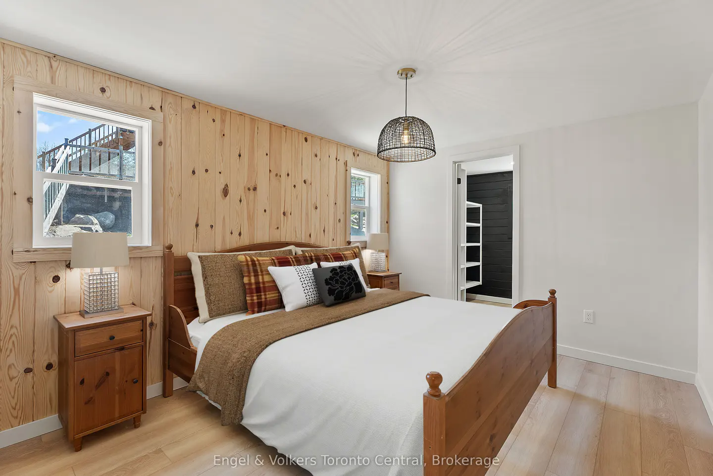 Bedroom with wood-paneled walls, a wooden bed with white linens, and a black wire pendant light.