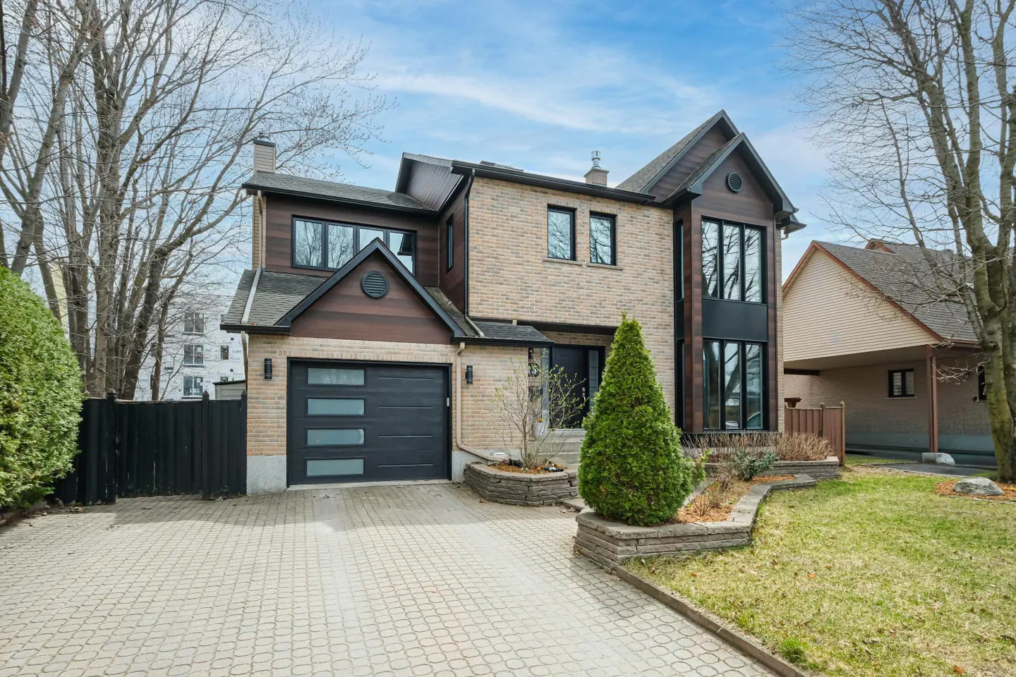 Two-story house with brick and wood siding, black garage door, and paved driveway on a cloudy day.