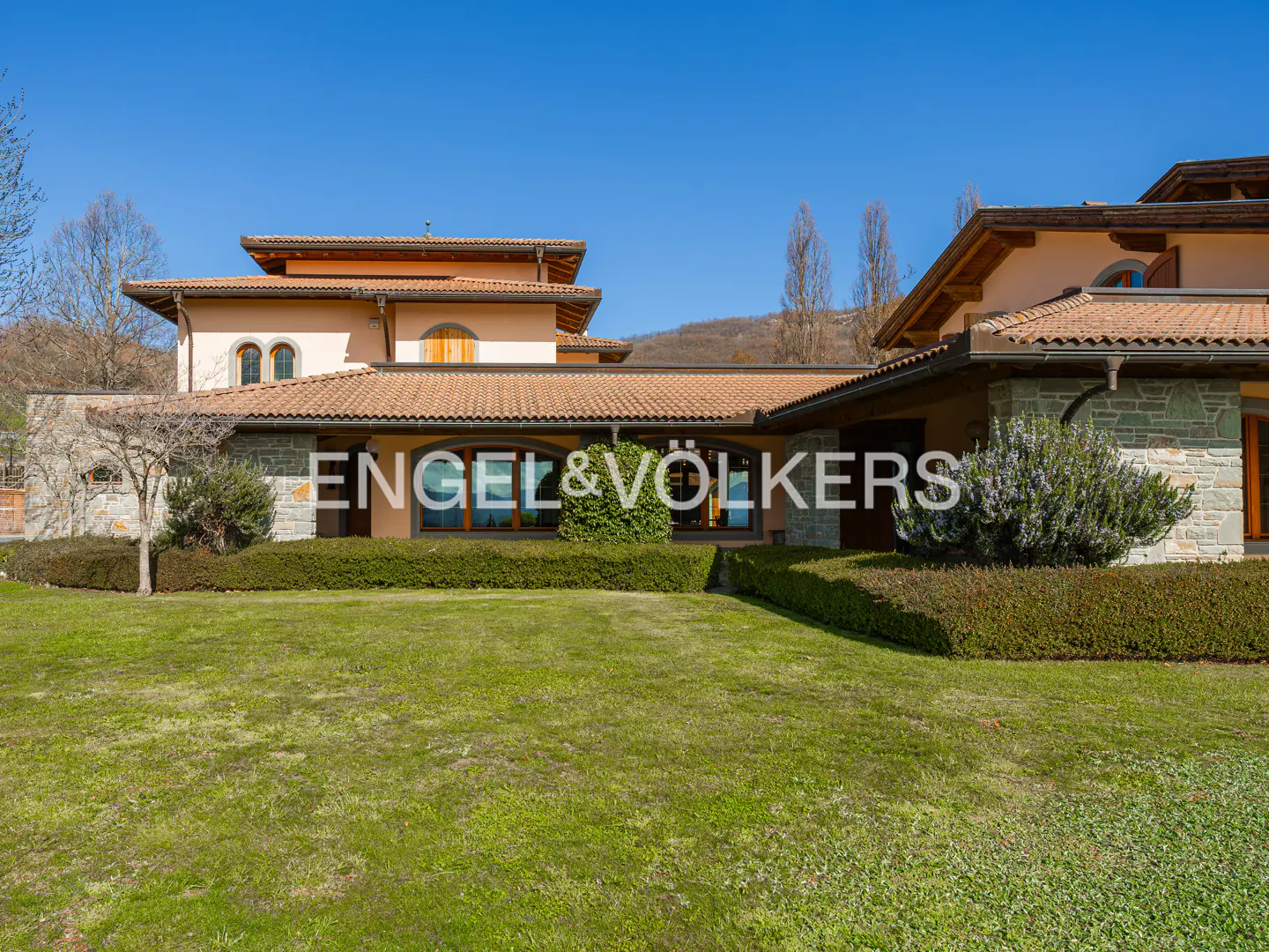 Exterior view of a peach-colored house with a brown tile roof and stone accents, set on a green lawn under a blue sky.