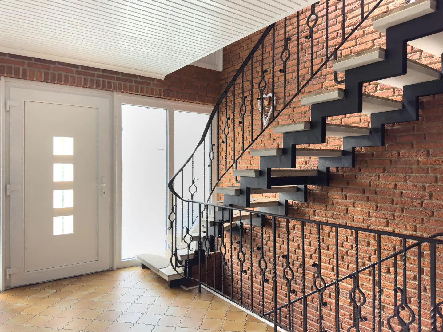 Entryway with a white door, brick wall, and modern staircase with black metal railings and light wood steps.