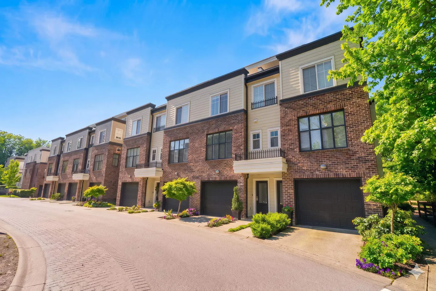 Row of brick townhouses with black garage doors and beige siding under a blue sky.