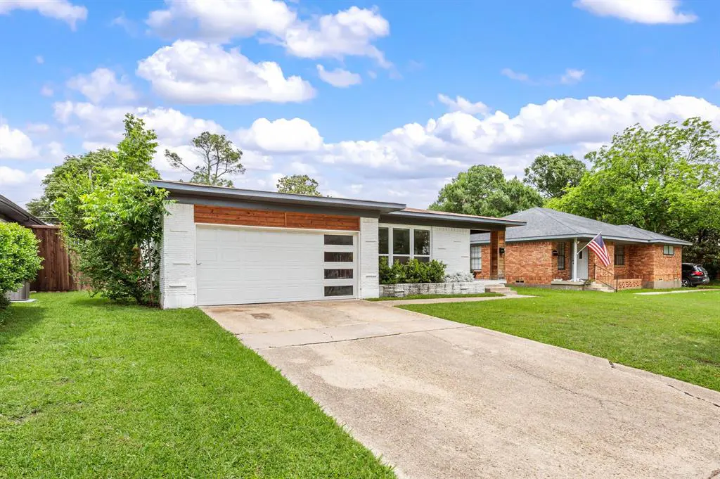 Exterior view of a white brick house with a white garage door and a concrete driveway. Blue sky with clouds in the background.
