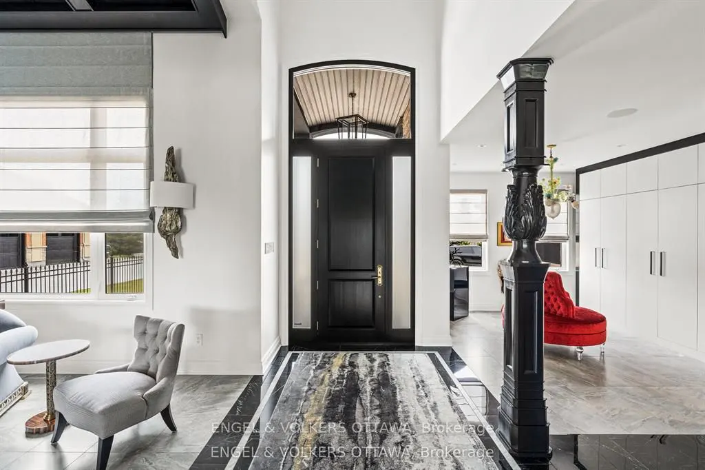 A bright foyer with a black front door, marble floors, and a decorative black column. A gray chair and red chaise lounge are visible.