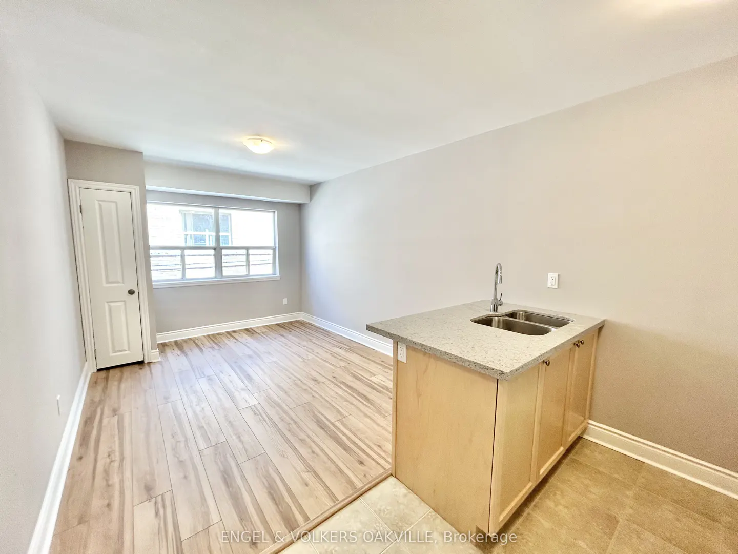 A bright, empty room with wood floors, a window, and a kitchen island with a sink.