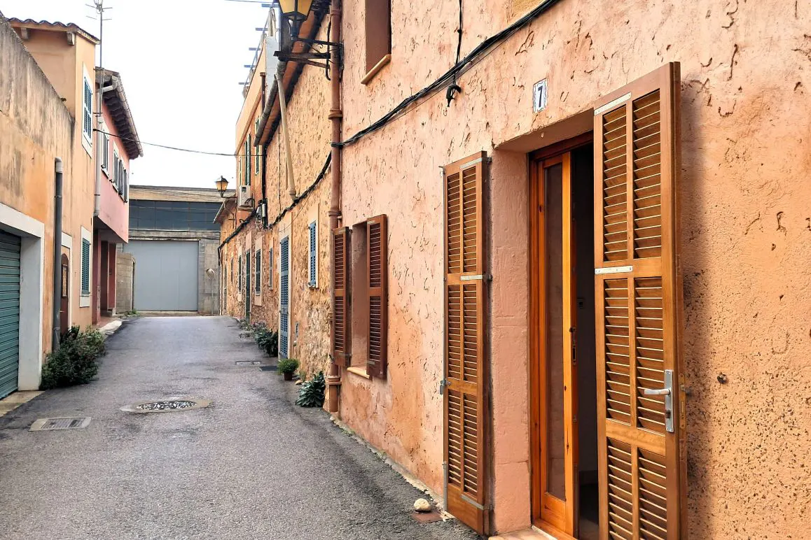 Narrow street view with peach-colored buildings, brown shutters, and a gray garage door in the background.
