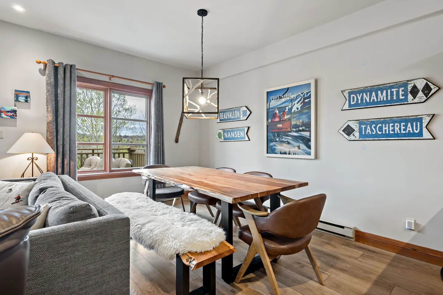 Living room with a wood table, bench with a white fur throw, and brown leather chairs. Ski-themed art hangs on the wall.