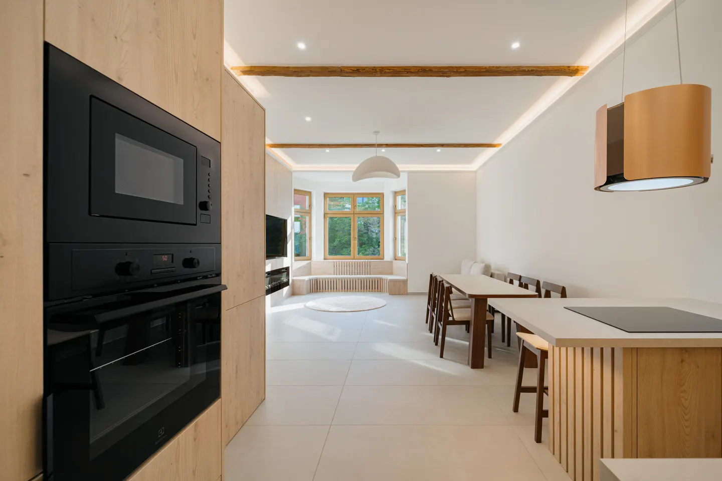 A bright, modern kitchen with black appliances, light wood cabinets, and a dining area with a large window.