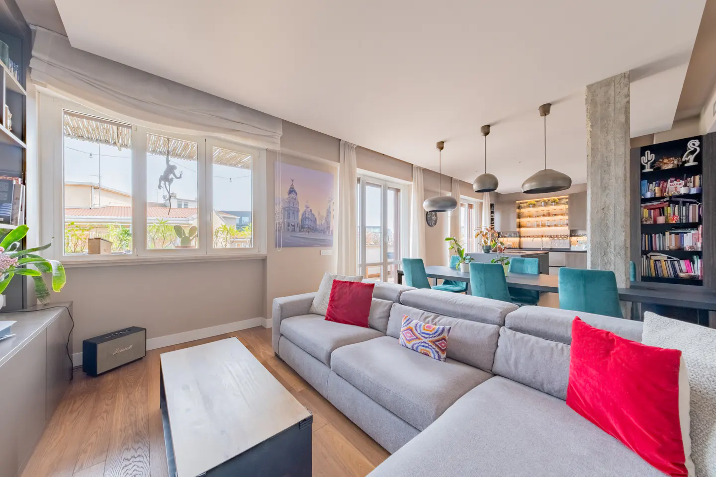 Modern living room with a grey sectional sofa, red accent pillows, a coffee table, and a dining area with teal chairs.