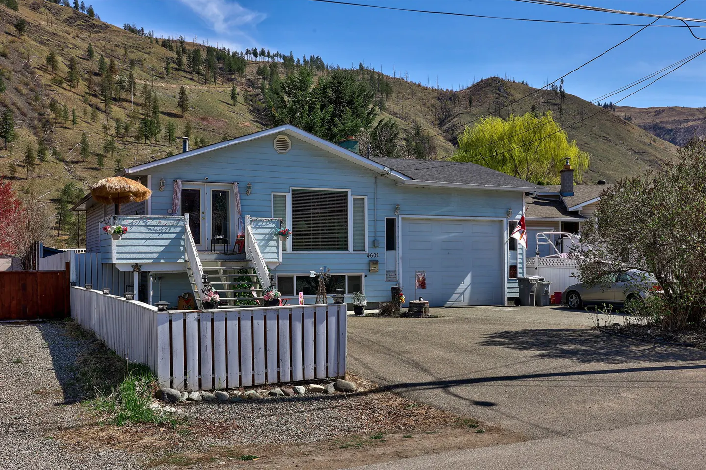 Light blue house with a white picket fence and a mountain backdrop on a sunny day.