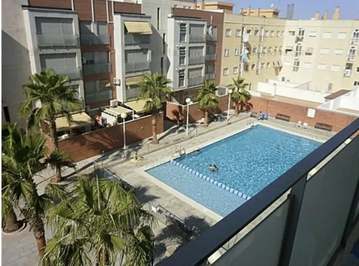Apartment complex with a blue swimming pool, palm trees, and buildings in the background.