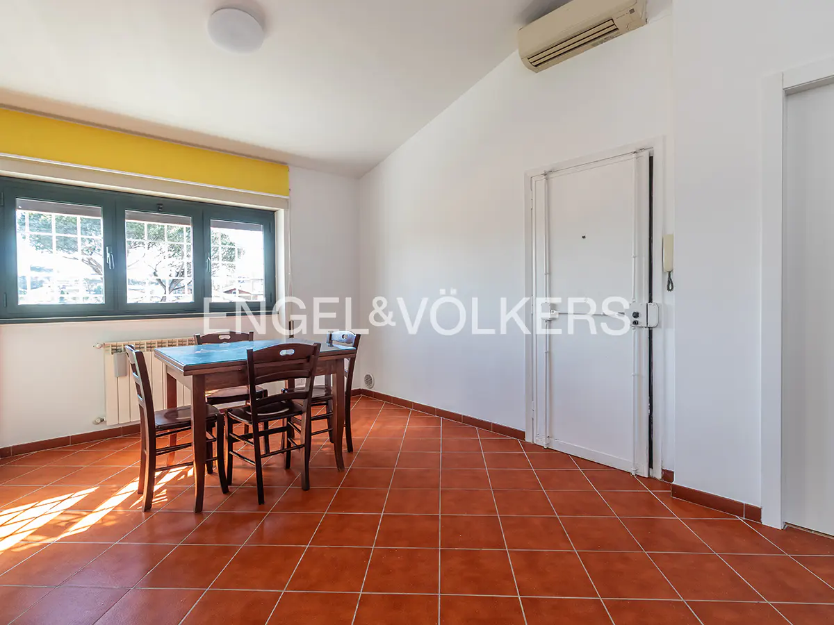 Bright room with terracotta tile floor, a dark wood table and chairs, and a large window with a yellow valance.
