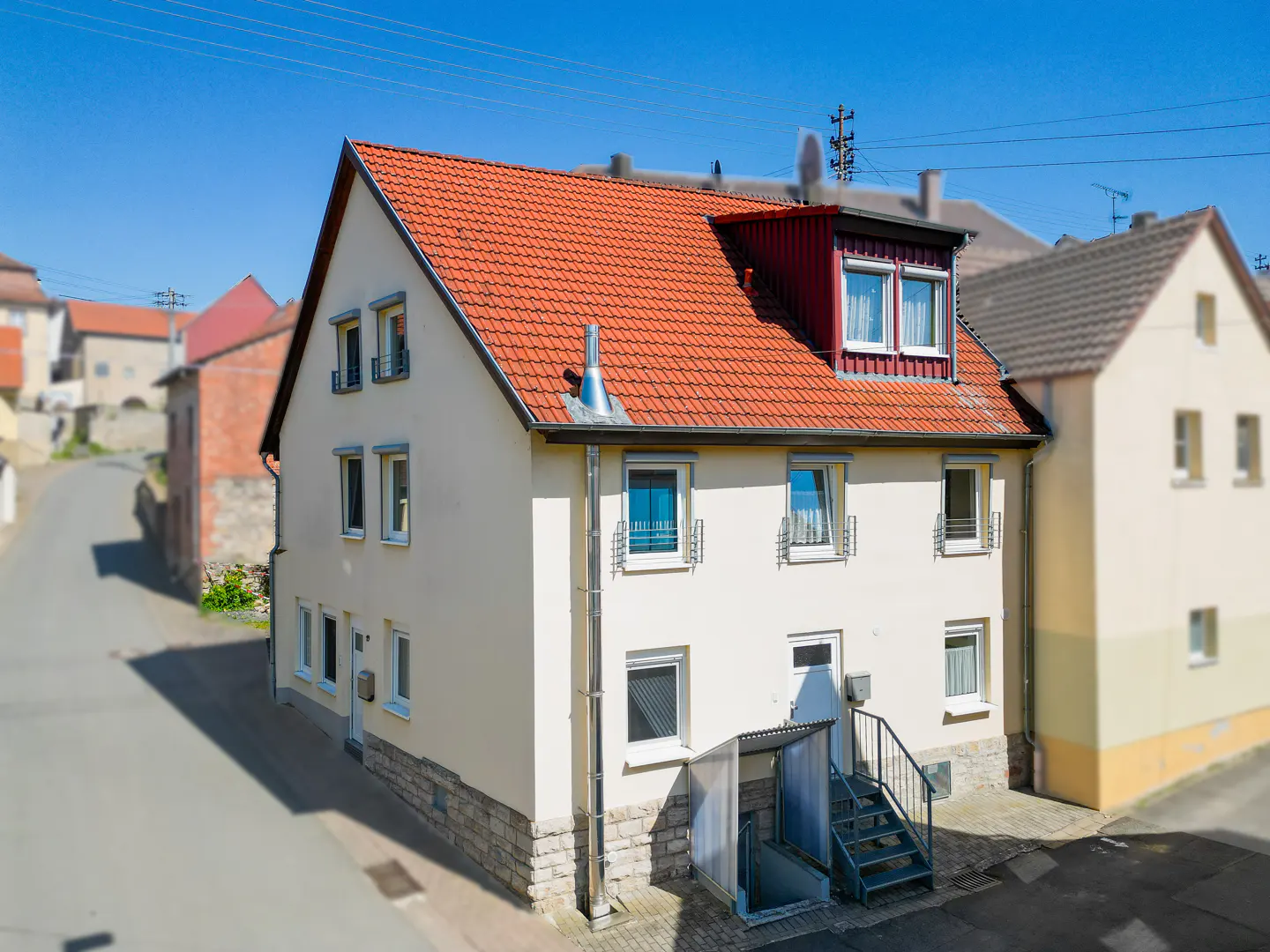 Two-story house with a red tile roof and a white facade, featuring a basement entrance with metal stairs.