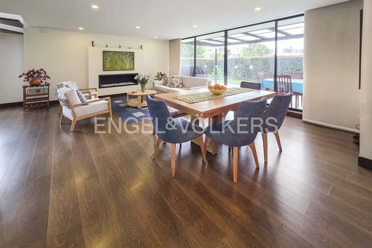 Open-concept living and dining area with wood floors, fireplace, and large windows overlooking the backyard.