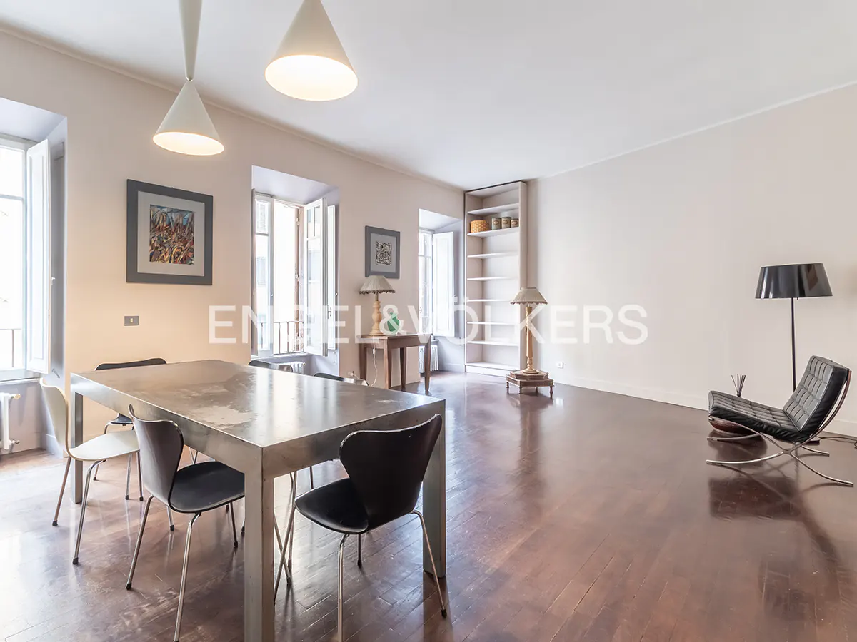 Modern dining room with a metal table, black chairs, hardwood floors, white walls, and a black lounge chair.