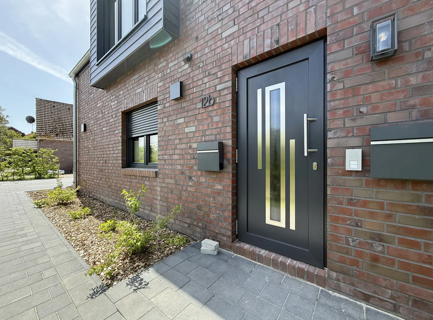 Brick house exterior with a black front door with gold accents, a mailbox, and a window with closed blinds.