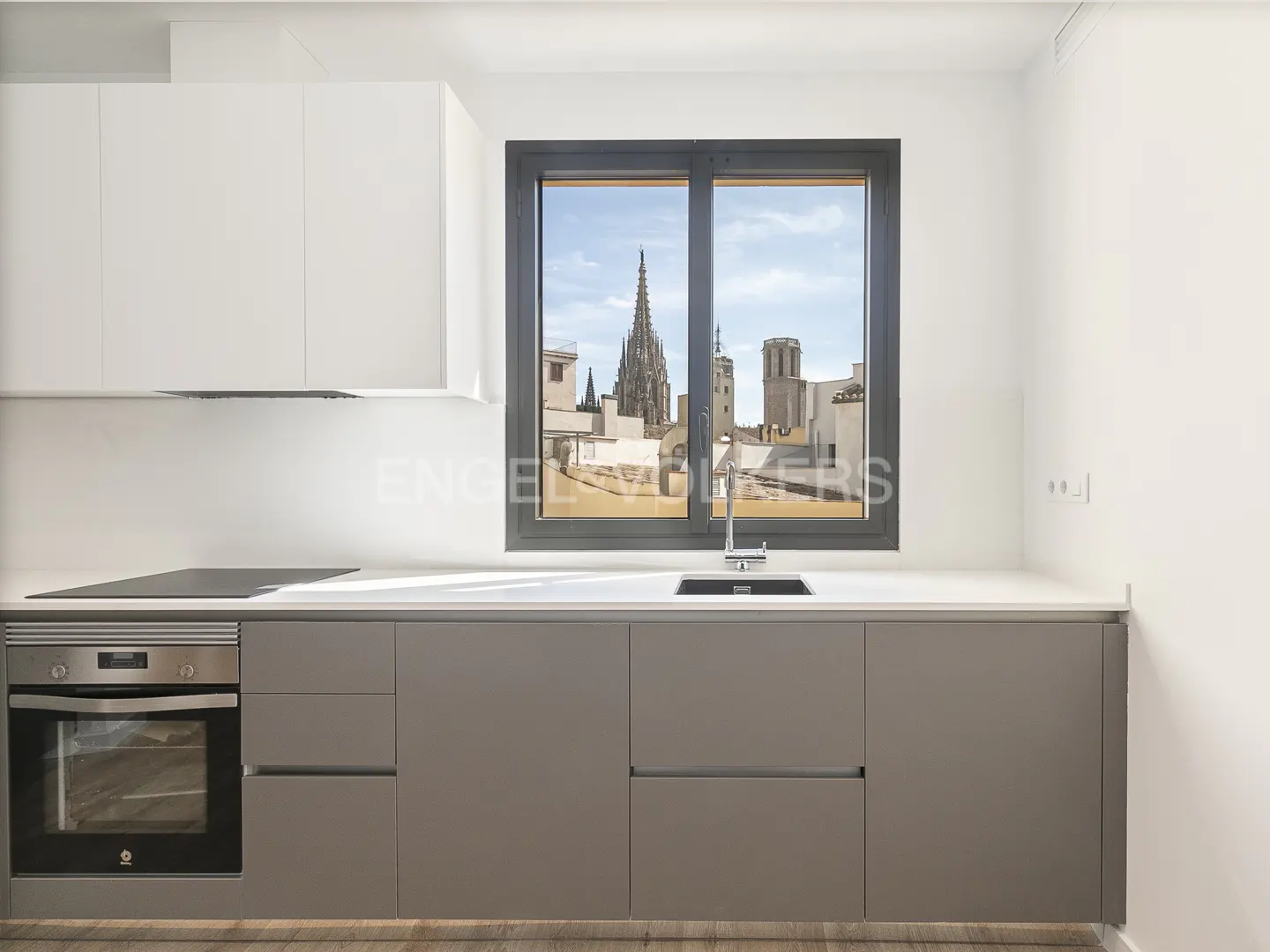 Modern kitchen with gray cabinets, white countertops, and stainless steel appliances. A window overlooks a city with a cathedral.