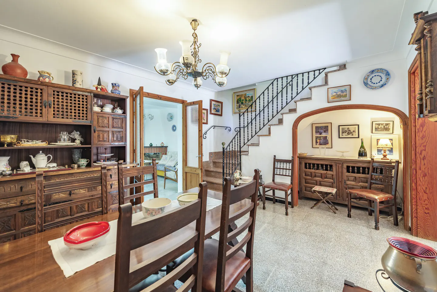 Dining room with wooden furniture, a chandelier, and a staircase leading to an upper floor with a tiled floor.