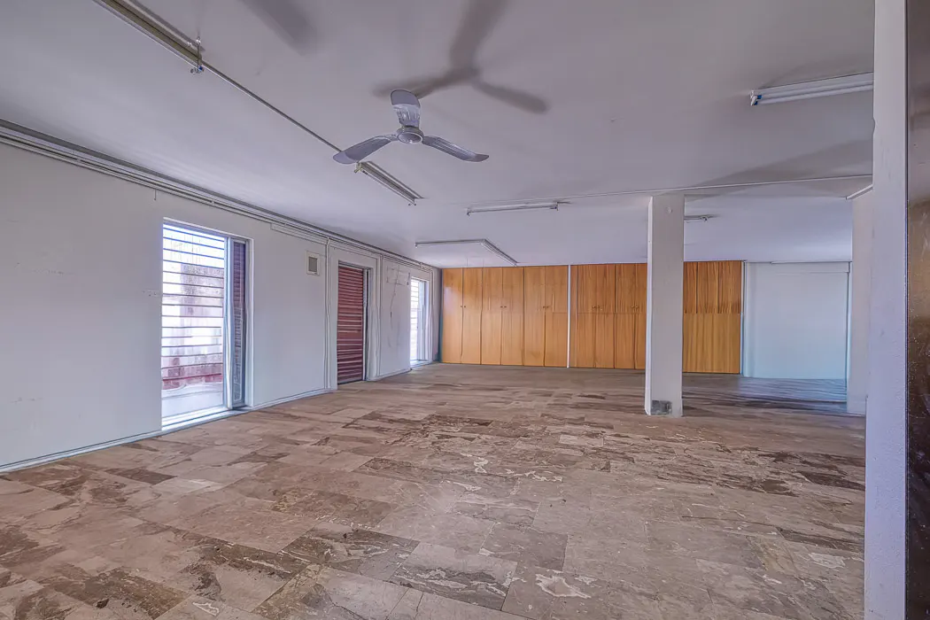 Empty room with white walls, a marble floor, and a ceiling fan. There are wooden cabinets on the back wall.