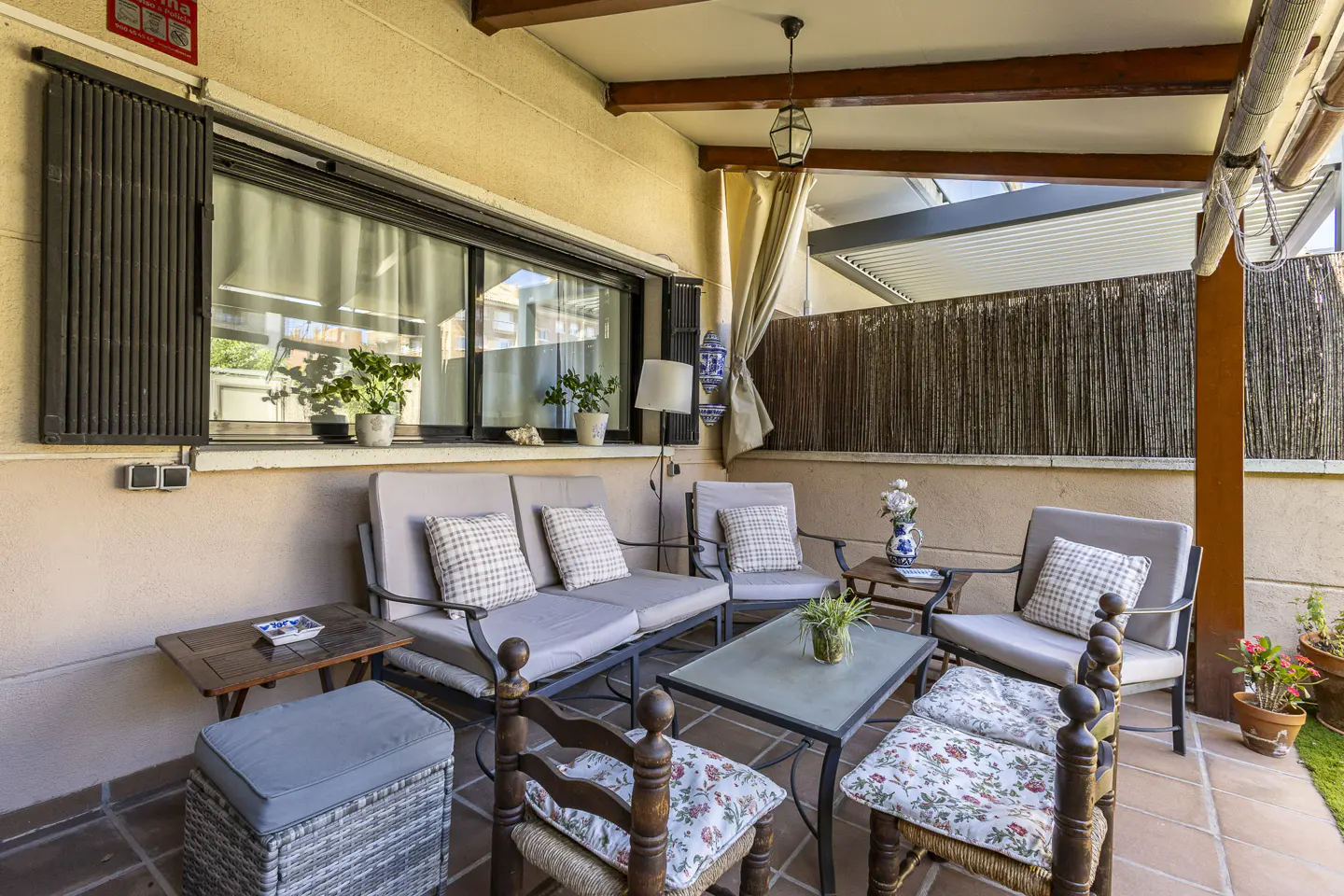 Covered patio with a sofa, armchairs, and a glass coffee table on a tiled floor, featuring a reed privacy fence.