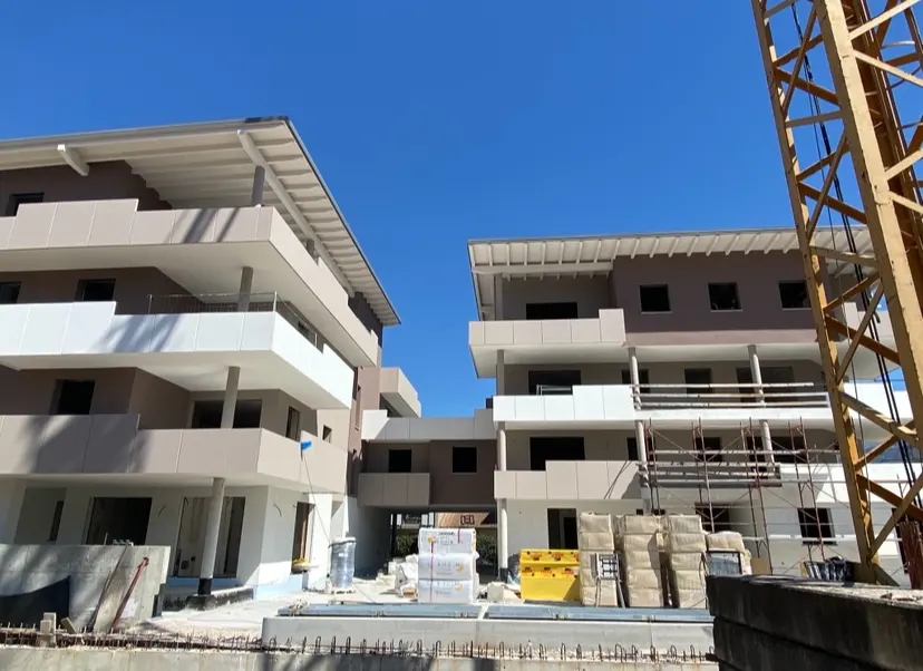 Construction site with two modern, multi-story buildings under a clear blue sky. A yellow crane is visible on the right.