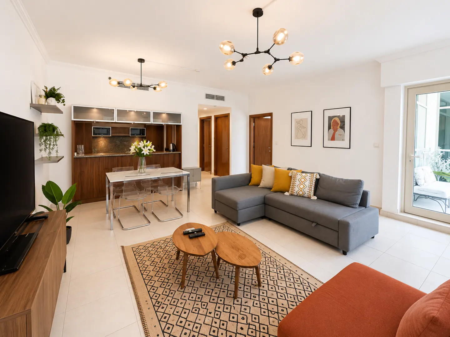 Modern living room with a grey sectional sofa, two wooden coffee tables, a dining area, and a patterned rug on white floors.