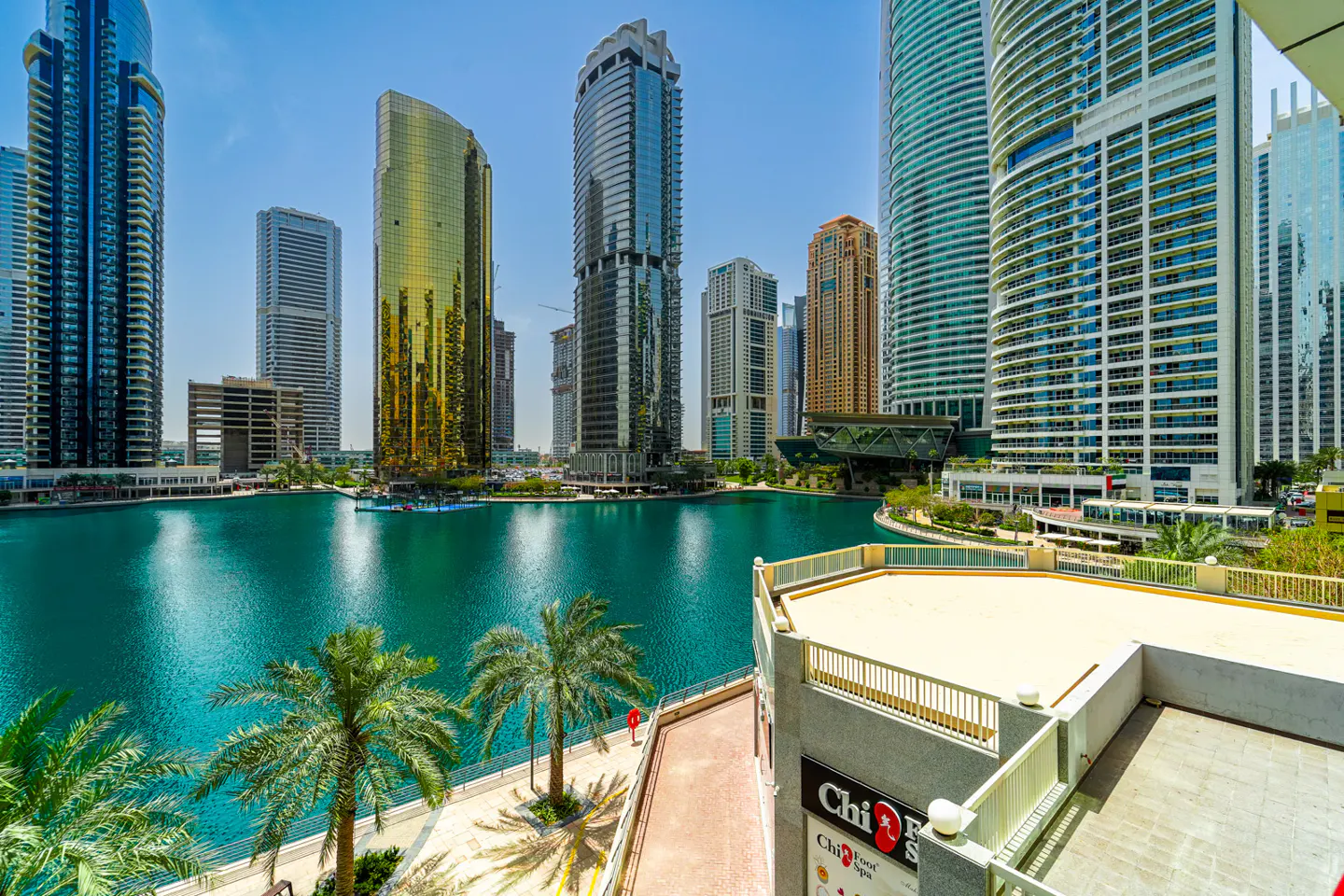 View of Dubai Marina with turquoise water, palm trees, and skyscrapers under a blue sky.