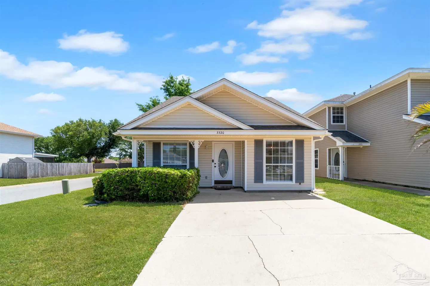 Beige single-story home with gray shutters, a white front door, and a concrete driveway under a blue sky with clouds.