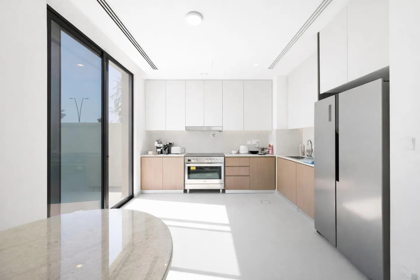 Modern kitchen with white upper cabinets, light wood lower cabinets, stainless steel appliances, and a large glass door.