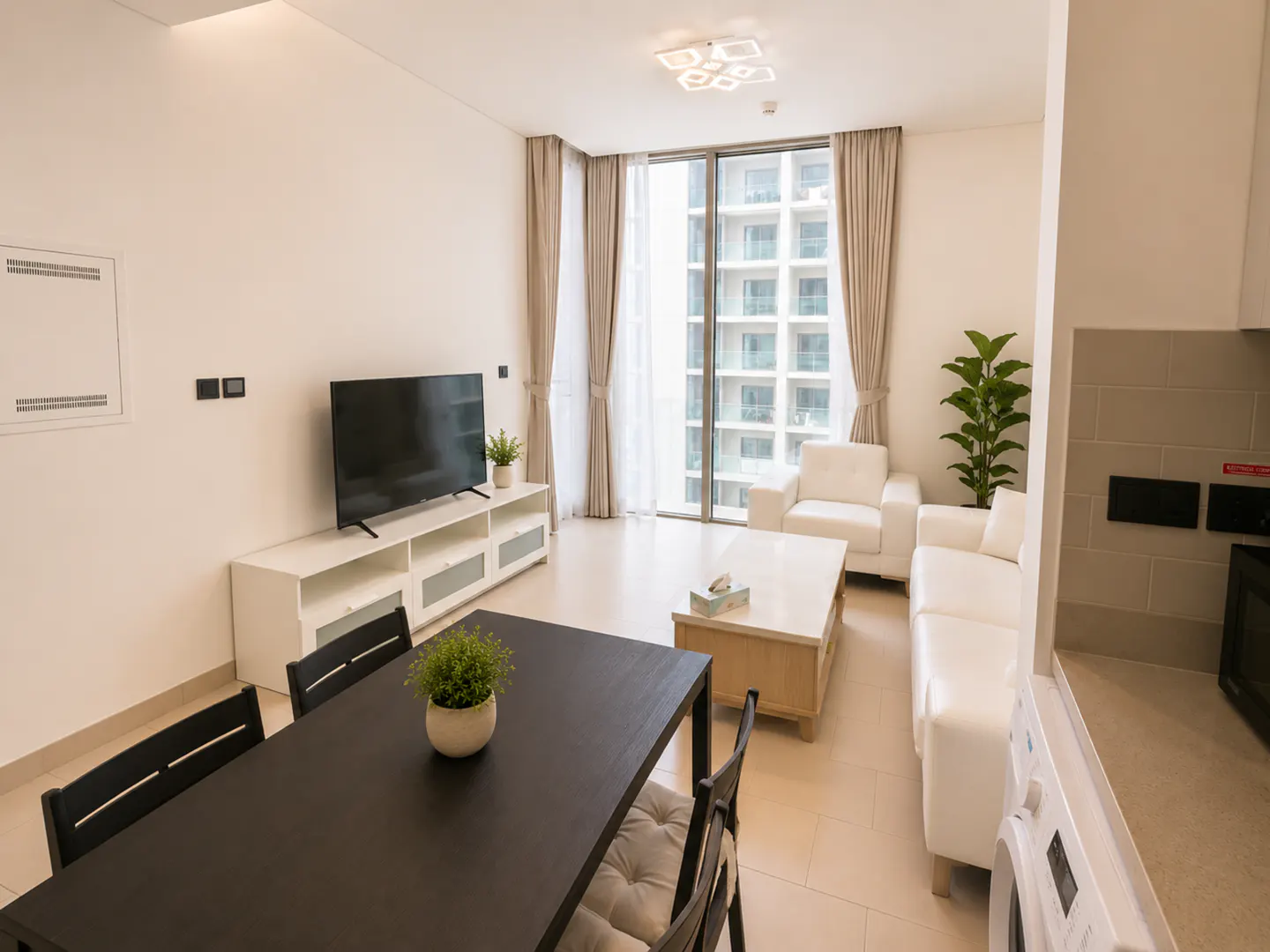 Bright apartment living room with a black dining table, white sofa and chairs, TV, and large window.