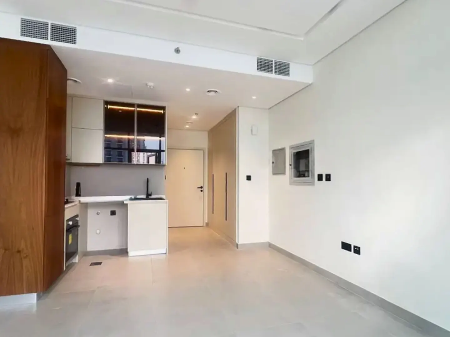 A bright, modern studio apartment with a kitchenette, white walls, and light gray flooring.