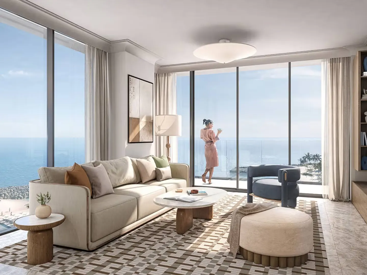 Bright living room with ocean view. A woman in a robe stands by the window. Beige sofa, blue chair, patterned rug.