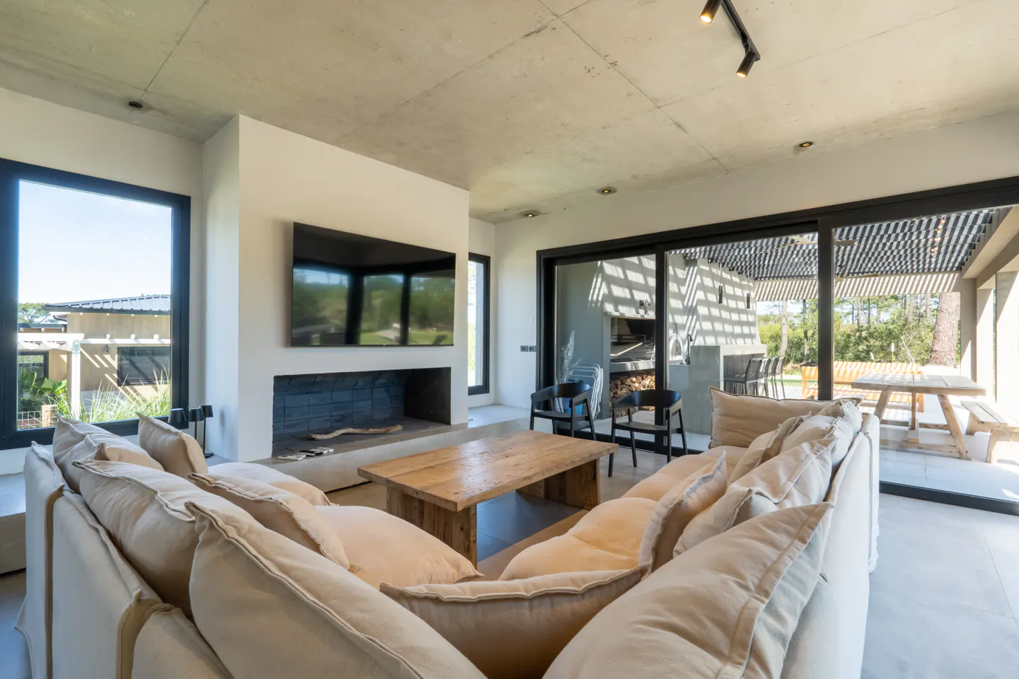 Bright living room with a large beige sofa, wooden coffee table, and fireplace with a TV above. Sliding glass doors lead to an outdoor patio.