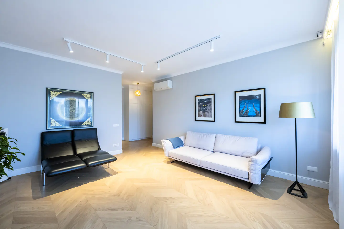 Bright living room with light gray walls, herringbone wood floors, white sofa, black chairs, and framed art.