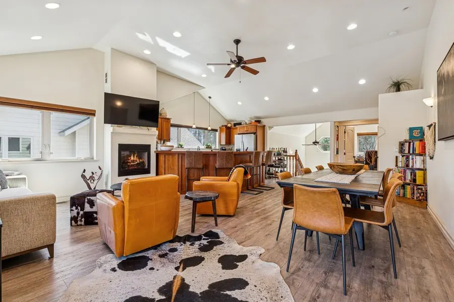 Open-concept living space with wood floors, vaulted ceilings, and a fireplace. Orange leather chairs and a cowhide rug add warmth.