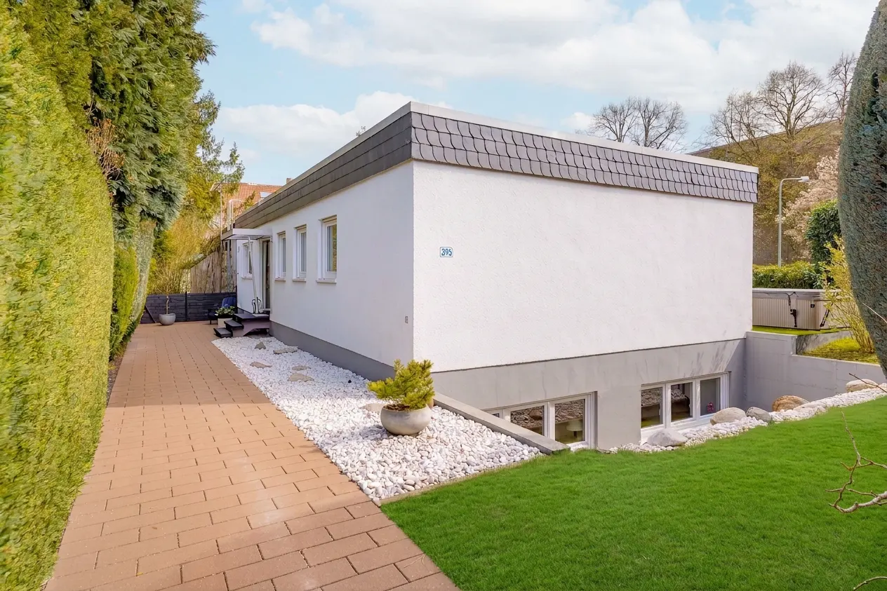Exterior view of a modern white house with a gray roof, green lawn, and brick walkway.