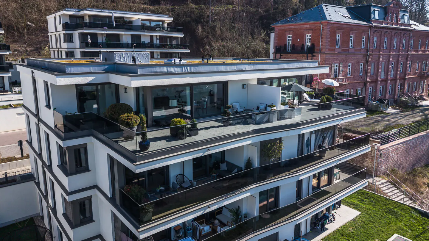 Modern white apartment building with glass balconies, next to an older red brick building and green lawn.