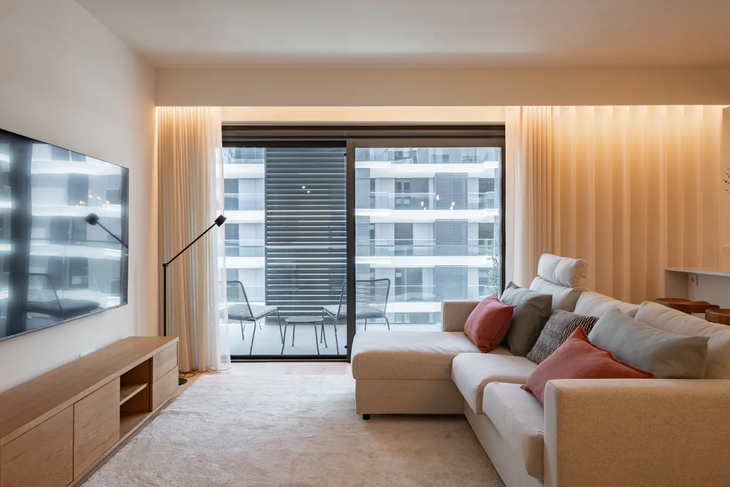 Modern living room with a beige sectional sofa, wooden media console, and large sliding doors opening to a balcony.