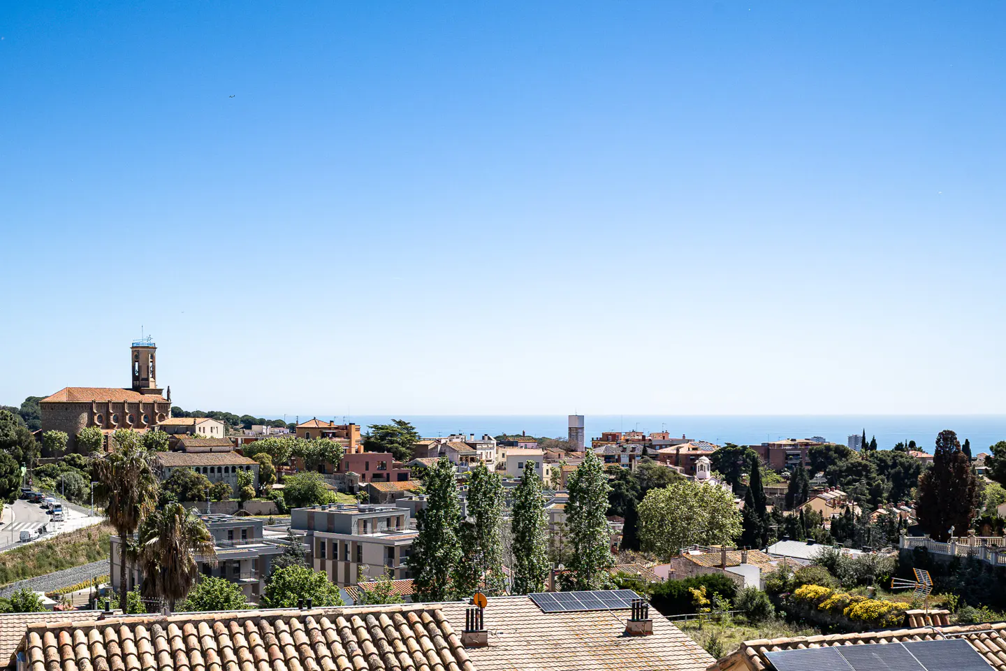 Scenic view of a coastal town with red-tiled roofs, a church with a tower, and the blue sea under a clear sky.