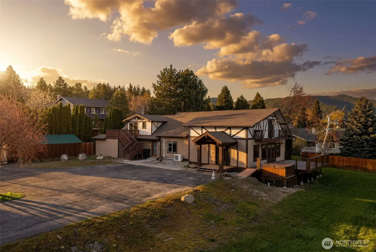 Exterior shot of a two-story home with a brown roof, white trim, and a hot tub on the deck. Trees and a cloudy sky are in the background.