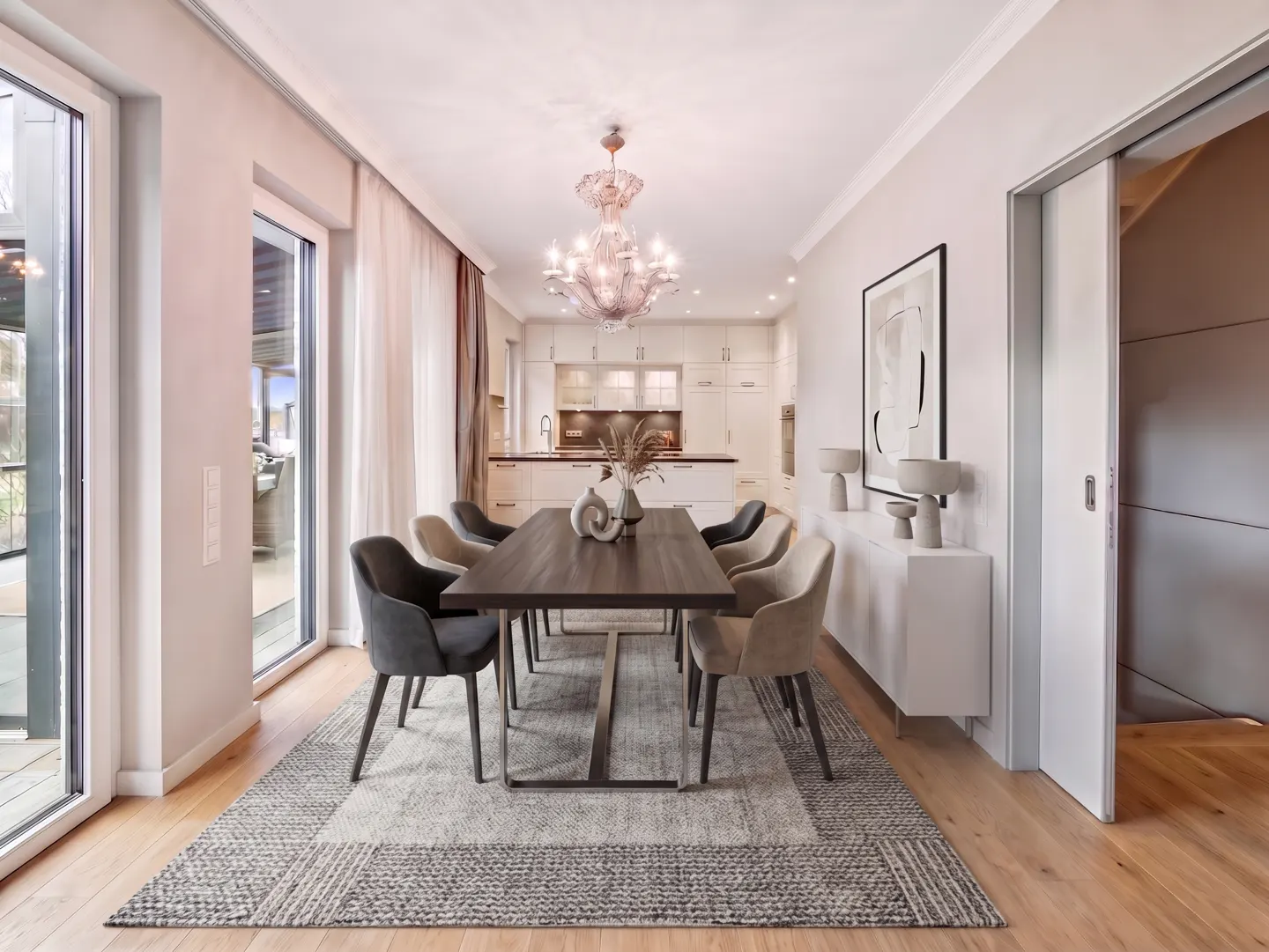 A dining room with a dark wood table, grey and beige chairs, and a large chandelier. The room has wood floors and a grey rug.