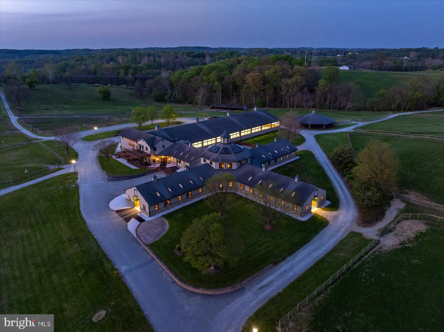 Aerial view of a horse farm at dusk, featuring a large complex with stables, a central circular building, and green pastures.