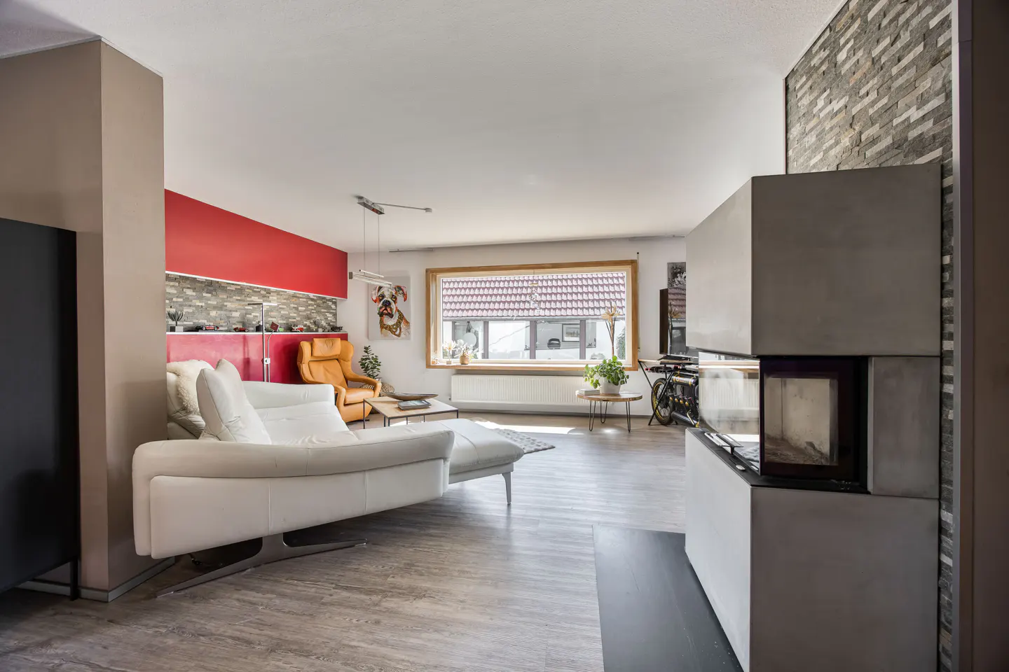 Bright living room with a white sofa, orange chair, and a modern fireplace with a stone accent wall. A window provides natural light.