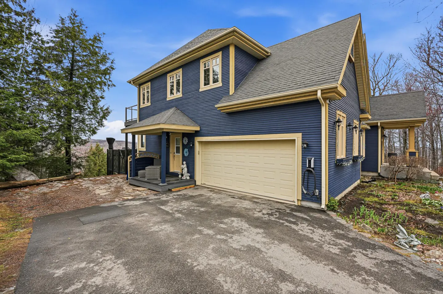Two-story blue house with tan trim, a gray roof, and an attached garage. A paved driveway leads to the house.