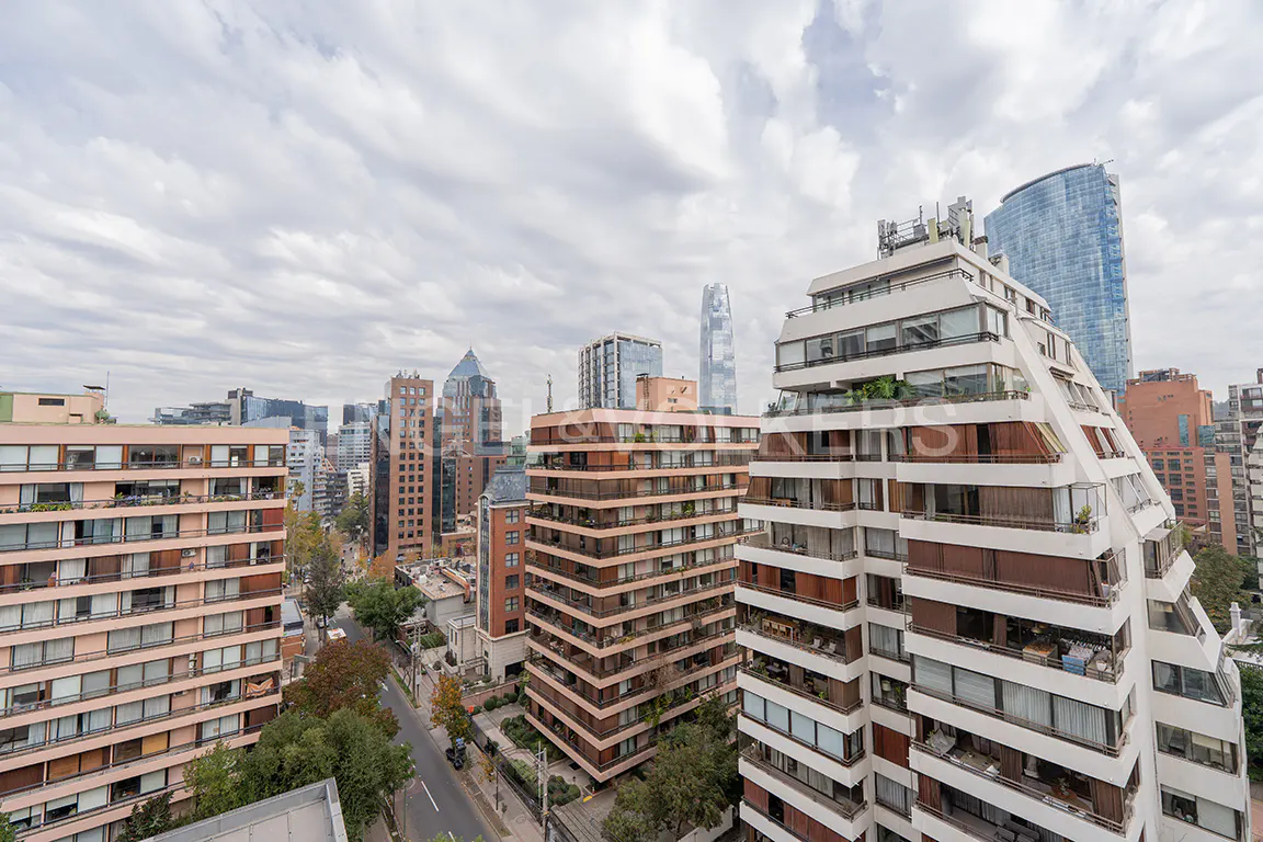Cityscape view with tall buildings, including a pyramid-shaped white apartment building and a blue glass skyscraper, under a cloudy sky.
