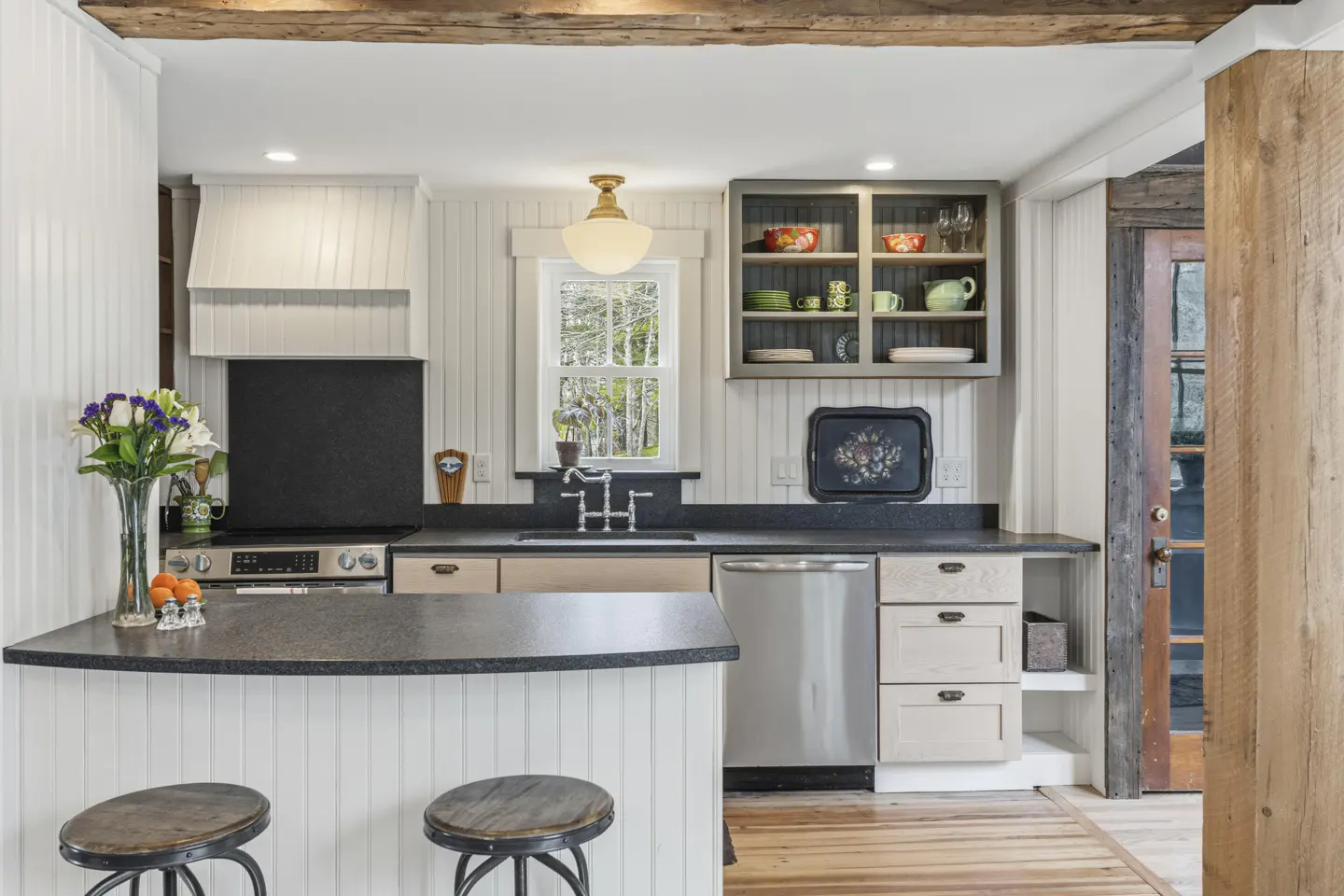 A bright kitchen with white walls, dark countertops, stainless steel appliances, and wooden accents.