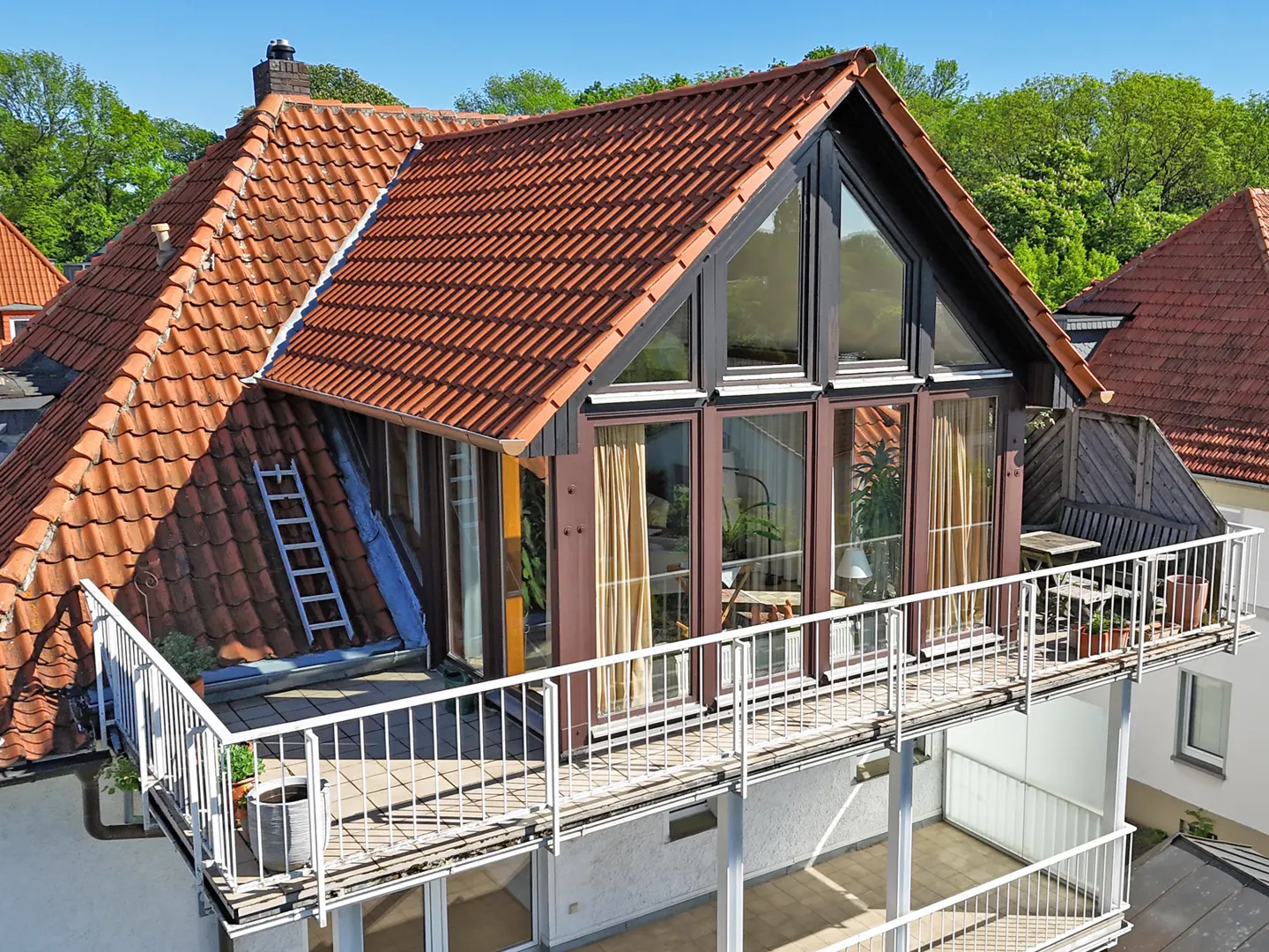 Exterior view of a house with a red tile roof and a balcony with white railings. Large windows offer views of the interior.