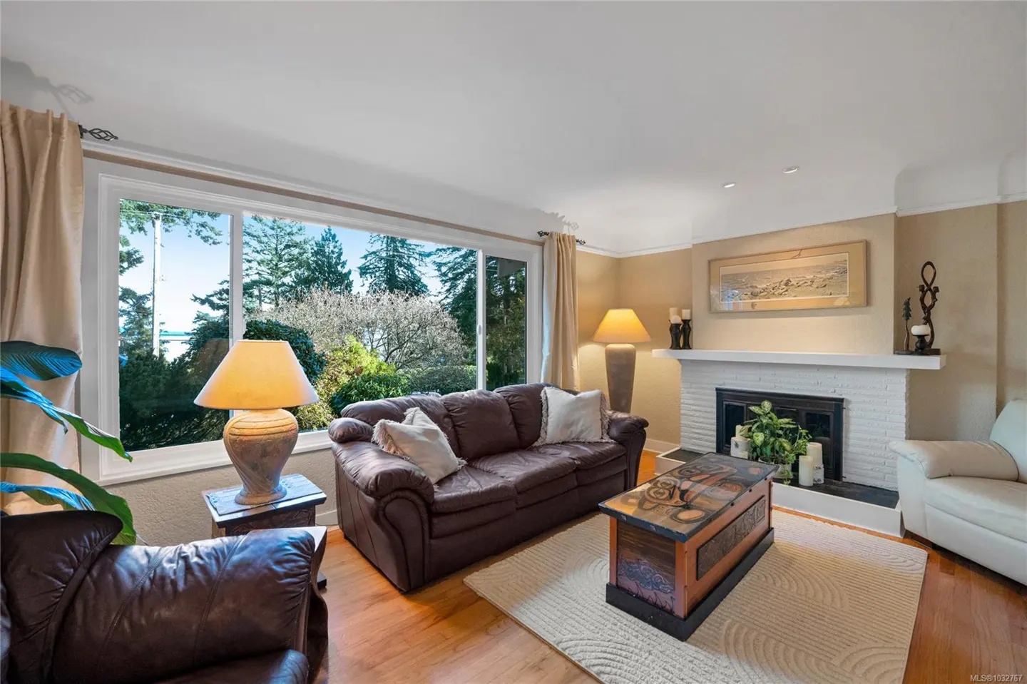 Living room with brown leather sofas, a white fireplace, and a large window with a view of trees and water.