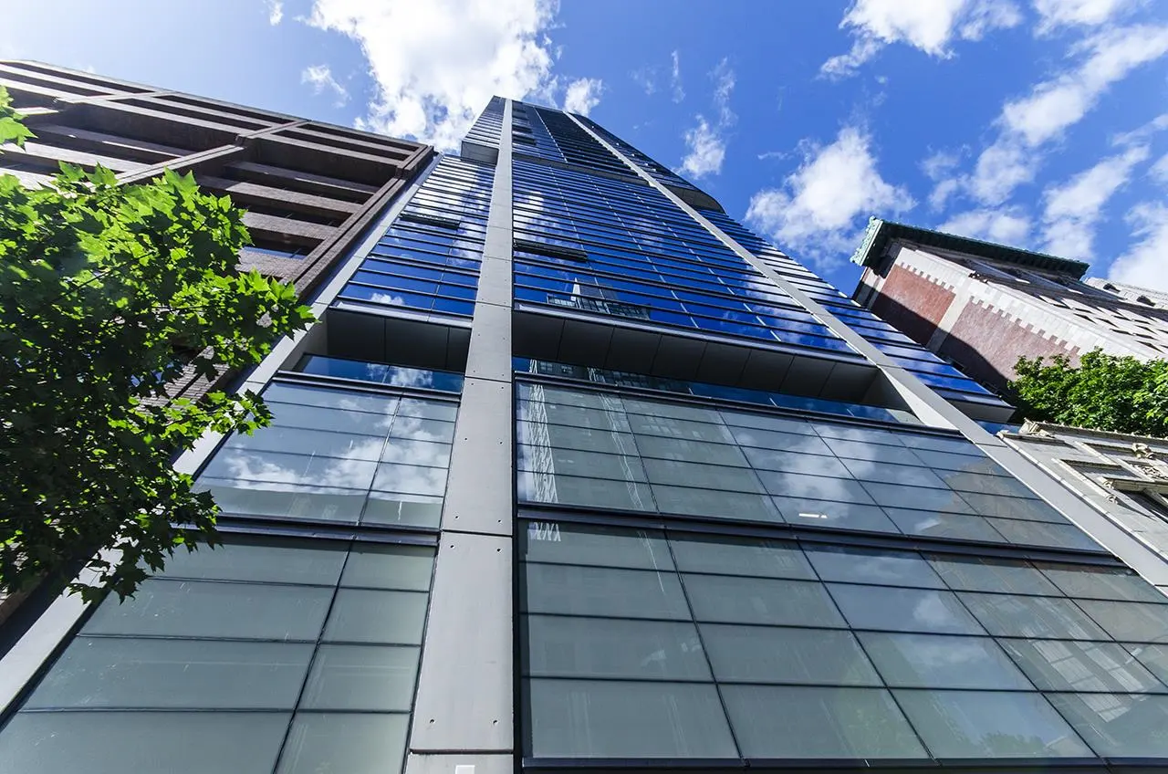 Low angle view of a tall, modern glass skyscraper with blue sky and clouds reflecting in the windows.