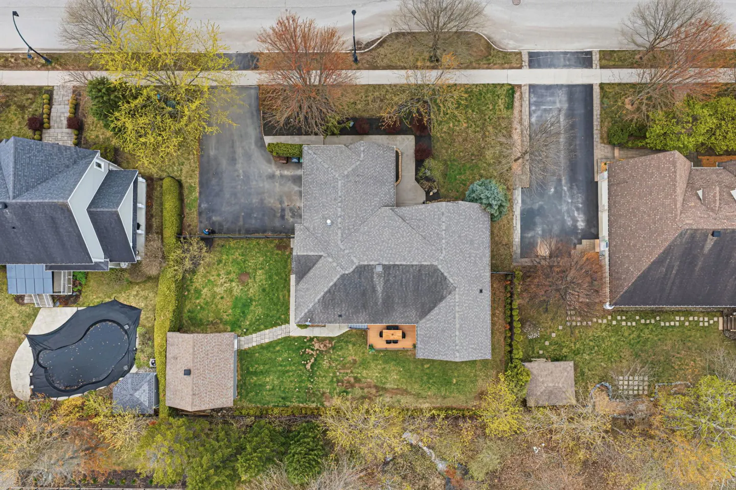 Aerial view of a gray roofed house with a driveway, green lawn, and a covered pool in the backyard.