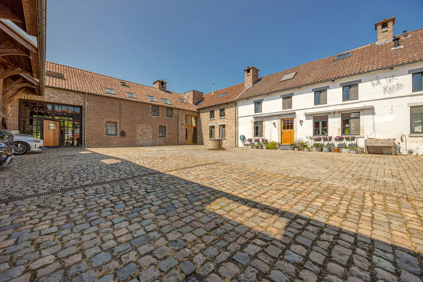 Cobblestone courtyard surrounded by a rustic brick and white-painted farmhouse under a clear blue sky.